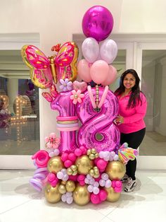 a woman standing next to a large pink and gold number balloon arrangement in front of a store window