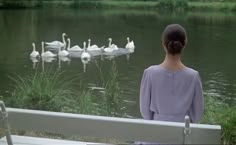 a woman sitting on a bench looking at swans