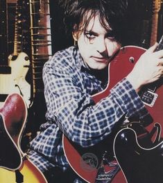 a man sitting in front of guitars holding his hand up to the guitar's neck