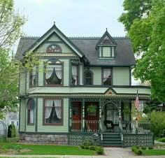 a large green house with two stories and a porch on the second story is surrounded by greenery