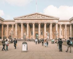 many people are walking around in front of a large building with columns and pillars on it