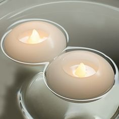 two lit candles sitting on top of a silver plate with water in the bottom bowl