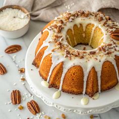 a bundt cake with white icing and pecans around it on a plate