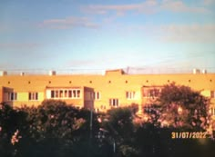 an orange building with trees in the foreground and blue sky behind it, on a sunny day