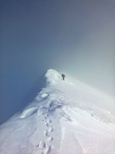 a person walking up the side of a snow covered mountain with footprints in the snow