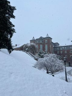 a snow covered hill with a building in the background and trees on both sides during a snowy day