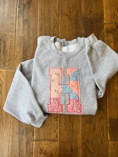 a child's sweatshirt with the letter h on it sitting on a wooden floor