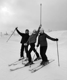 three people on skis posing for the camera with their arms up in the air