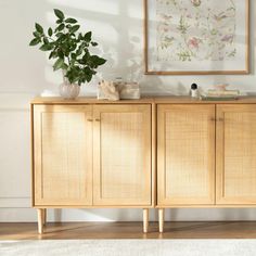 a wooden sideboard with plants and pictures on the wall