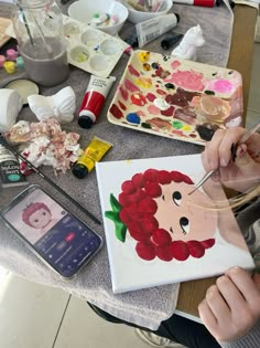 a woman is painting on a canvas with flowers and other crafting supplies around her