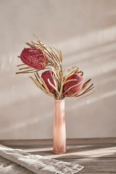 a vase filled with dried flowers on top of a wooden table next to a napkin