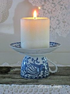 a lit candle sitting on top of a blue and white plate next to a lace doily