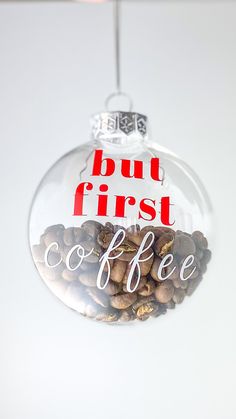 a glass ornament with coffee beans hanging from it's side and the words but first coffee in red