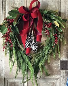 a christmas wreath hanging on a door with red ribbon and pine cones, evergreen leaves and berries