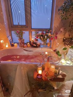 a bath tub with candles and flowers on it in front of a window filled with windows