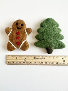 two small felt christmas trees next to a measuring ruler on a white surface, one has a ginger and the other has a gingerbread