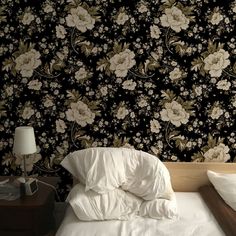 an unmade bed in front of a black floral wallpaper with white flowers on it