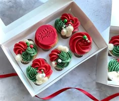 cupcakes decorated with red, green and white frosting in a box on a table