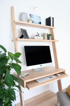 a computer desk with a monitor and keyboard sitting on it's stand next to a potted plant