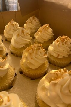 cupcakes with white frosting and gold sprinkles in a box