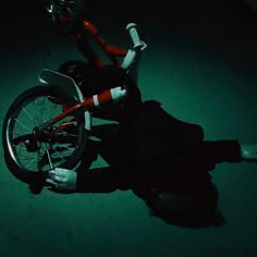 a person laying on the ground next to a bike in the dark with their legs spread out