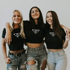 three young women standing next to each other in front of a white wall wearing black t - shirts