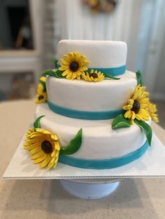 a three tiered cake with sunflowers on the top and blue ribbon around it