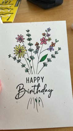 a hand holding a card with flowers on it that says happy birthday written in black ink