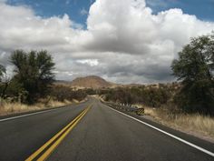 an empty road with mountains in the background and clouds in the sky above it on a sunny day