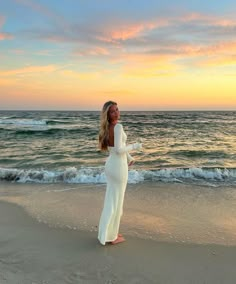 a woman standing on top of a sandy beach next to the ocean at sun set