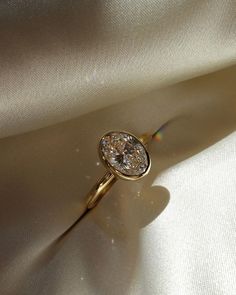 a diamond ring sitting on top of a white satin surface with sunlight shining through it