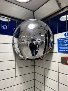 a mirror hanging on the wall in a subway station with people walking by and another person standing next to it