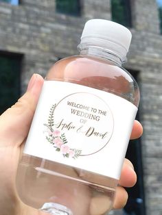 a person holding a bottle of water in front of a brick building that says, welcome to the wedding of ashton and barn