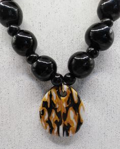 I've used the Japanese mokume gane technique to create this polymer clay pendant. It comprises gold, black and white polymer clay. The pendant has been teamed with chunky black glass beads and smaller wooden beads.  I chose white beads so that the marbled pendant would really stand out. (And I'm a big fan of the chunky!) The necklace is closed with a lobster claw lock and extends to 49cm maximum with use of the extender chain. Use the lobster claw to meet the length that best suits you. The pend Unique Black Necklace With Large Pendant, Adjustable Black Medallion Necklace, Black Necklace With Detachable Pendant, Adjustable Black Necklace, Adjustable Black Medallion Jewelry, Artisan Black Pendant Jewelry, Unique Black Round Pendant Jewelry, Black Amulet Necklace With Large Pendant, Black Medallion Shaped Jewelry For Jewelry Making