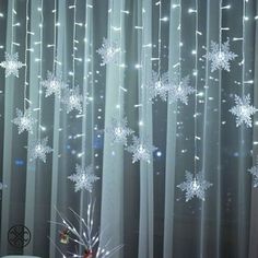 snowflakes are hanging from the sheer curtain in this room with white curtains and lights