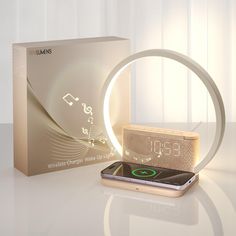 an alarm clock is sitting next to a box on a white table top with a cell phone in front of it