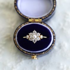 an antique diamond and pearl ring in a blue velvet box on a white marble surface