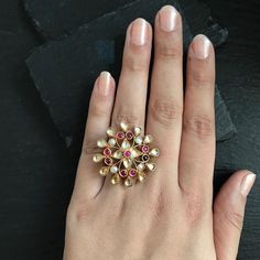 a woman's hand with a ring on it that has various colored stones in the middle