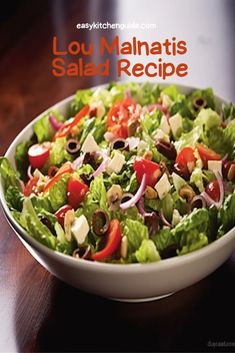 a salad with lettuce, tomatoes and olives in a white bowl on a wooden table