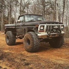 an old black truck is parked in the woods