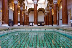 an indoor swimming pool surrounded by columns and pillars in a large room with marble flooring