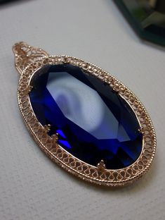 large sapphire blue gem oval pendant with rose gold art deco filigree Formal Sapphire Pendant Jewelry, Sapphire Gemstone Art Deco Jewelry, Elegant Faceted Sapphire Necklaces, Luxury Sapphire Art Deco Jewelry, Exquisite Sapphire Pendant Necklace, Art Deco Brooch, Gold Art Deco, Art Deco Necklace, Sapphire Pendant