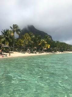 people are on the beach in front of palm trees and water with mountains in the background