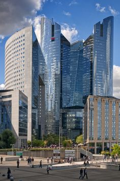 many people are walking around in front of some very tall buildings with skyscrapers behind them