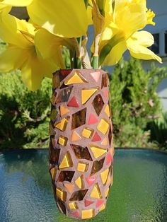 a vase with yellow flowers in it sitting on a table next to some water and grass