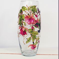 a glass with flowers painted on it sitting on a white table next to a wall