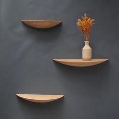 three wooden shelves with vases and flowers on them against a gray wall behind it