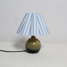 a lamp with a blue and white striped shade sitting on top of a table next to a wall