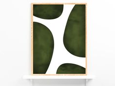 a green and white abstract art print on a wooden frame hanging on a wall next to a shelf