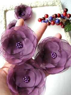 three purple flowers sitting on top of a white table next to a beaded bracelet